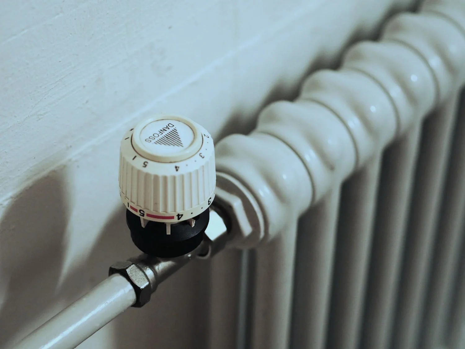 Weisser Radiator mit Thermostatventil an der Raumwand.